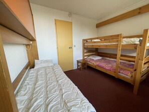 A room with a bunk bed, a single bed, a door, and a small table.