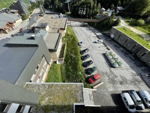 An aerial view of a parking lot with several cars, a building with a sloped roof, and a green area with trees.