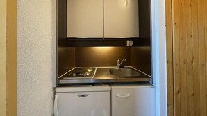 A compact kitchenette with a stove, sink, and white cabinets. - 10m from ski slopes, 6th floor, view valley, balcony, tv, 18m², Les Menuires (Les Menuires)