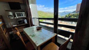 A small dining area with a table and chairs, a microwave, a coffee maker, and a view of a mountainous landscape through a balcony. - 10m from ski slopes, 6th floor, view valley, balcony, tv, 18m², Les Menuires (Les Menuires)