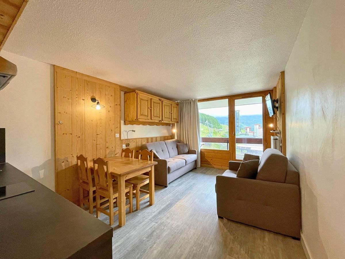 A cozy room with a wooden dining table, a sofa, and a large window offering a view of the outdoors.