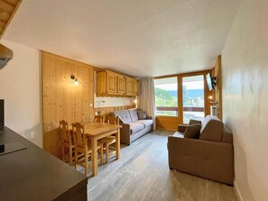 Une pièce chaleureuse avec une table à manger en bois, un canapé et une grande fenêtre donnant sur l’extérieur.