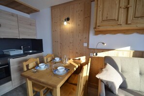 Une cuisine compacte avec des meubles en bois, une table à manger pour quatre personnes et un canapé dans le salon attenant.