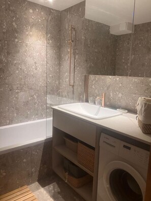 Ein modernes Badezimmer mit einem großen Waschbecken, einer Duschkabine aus Glas, einer Bosch Waschmaschine und einem Spiegel über dem Waschbecken.