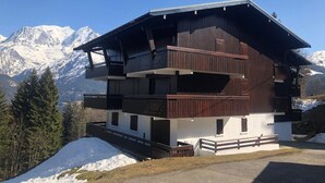 Una chaleta de varios pisos con balcones, con montañas nevadas al fondo.