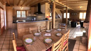 Interior de una cabaña de madera con comedor para cuatro, una cocina con isla central y una escalera que conduce a un nivel superior.