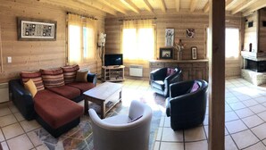Acogedor interior de cabaña de troncos con sofá, sillones, televisor y chimenea.