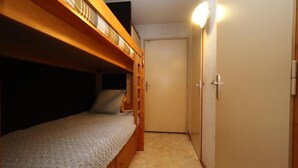 A narrow room with a bunk bed, a door, and a light fixture.