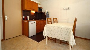 A compact kitchen with wooden cabinets, a refrigerator, a microwave, and a dining table with chairs.