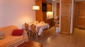 Ein gemütliches Wohnzimmer mit einem gestreiften Sofa, einem Esstisch mit Stühlen und einer Küchenzeile mit Holzschränken und einem Herd.