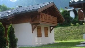 Eine Chalet mit Holzbalkon, Steinmauer und Rasenfläche.
