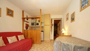 Ein gemütlicher Raum mit einem roten Sofa, einem Bett mit sternenbesetzter Bettdecke, einer Küchenzeile mit einer Mikrowelle und einer Holztür, die in einen anderen Raum führt.