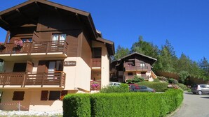 Ein Chalet mit Balkonen, einem Schild mit der Aufschrift „le bruyères“ und einem Parkplatz mit Autos.
