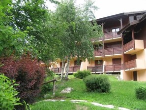 A multi-story building with balconies, surrounded by lush greenery and a well-maintained garden.