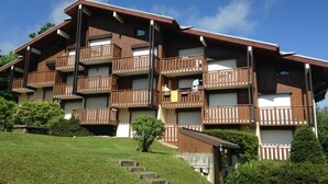 Un edificio a più piani con balconi, un prato davanti e cielo sereno.