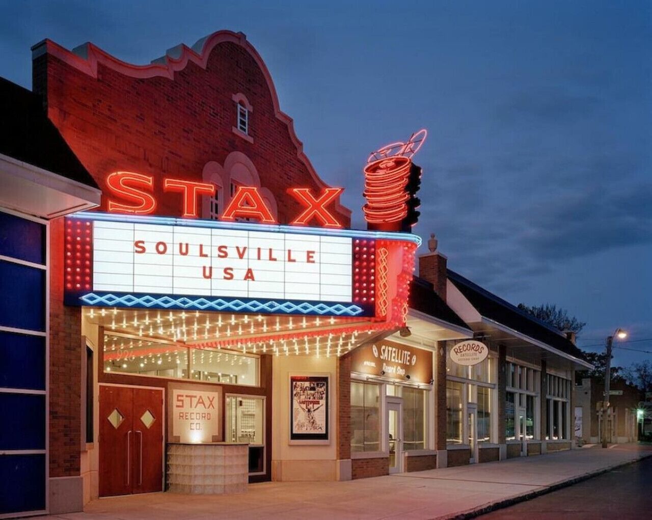 Un teatro con un letrero de neón que dice "STAX SOULSVILLE USA" y una tienda satélite cercana.