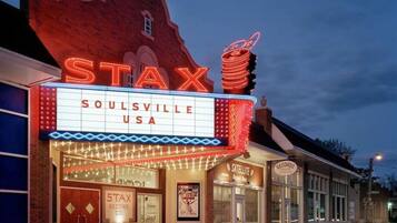 Un teatro con un letrero de neón que dice "STAX SOULSVILLE USA" y una tienda satélite cercana.