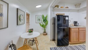 Cocina compacta con refrigerador, gabinetes de madera, cafetera y una pequeña mesa de comedor con sillas.