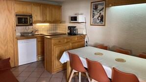 Een praktische keuken met houten kastjes, een magnetron, een koffiezetapparaat en een eethoek met een tafel en stoelen.