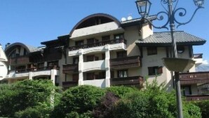 A multi-story building with balconies, a street lamp, and lush greenery in front.