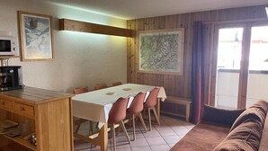 Een gezellige woonkamer met een houten eettafel, een bank en een keukenhoek met een magnetron en koffiezetapparaat.