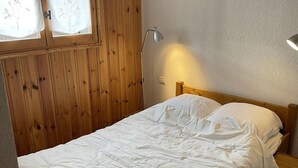 Een slaapkamer met een houten hoofdbord, een enkel bed met witte beddengoed, een nachtkastje met een lamp en een raam met geëtste glas.