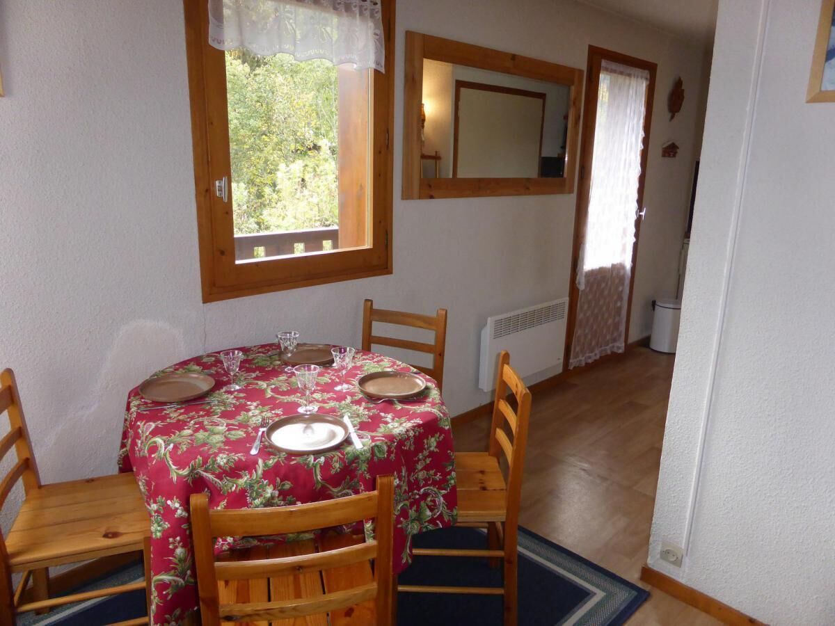Una zona de menjador amb una taula rodona preparada per a quatre persones, una finestra amb vistes a vegetació i un mirall a la paret.