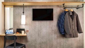 A hotel room with a bed, a desk with a laptop, a TV mounted on the wall, and a coat rack with two coats. - ibis budget Manchester Airport (Manchester)