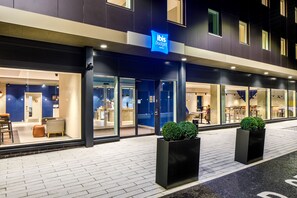 A modern hotel exterior with a blue sign, glass doors, and outdoor seating. - ibis budget Manchester Airport (Manchester)