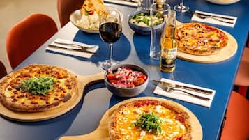 Una mesa de comedor con pizzas, un tazón de ensalada y una botella de cerveza Corona Extra.