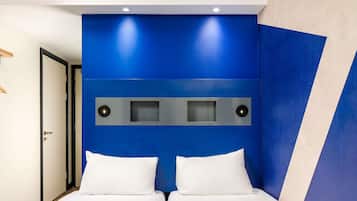 A hotel room with a blue accent wall, a bed with white bedding, and a door to the left.