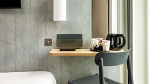 A modern hotel room with a concrete wall, a wooden desk with a laptop, a coffee maker, and a black chair. - ibis budget Manchester Airport (Manchester)