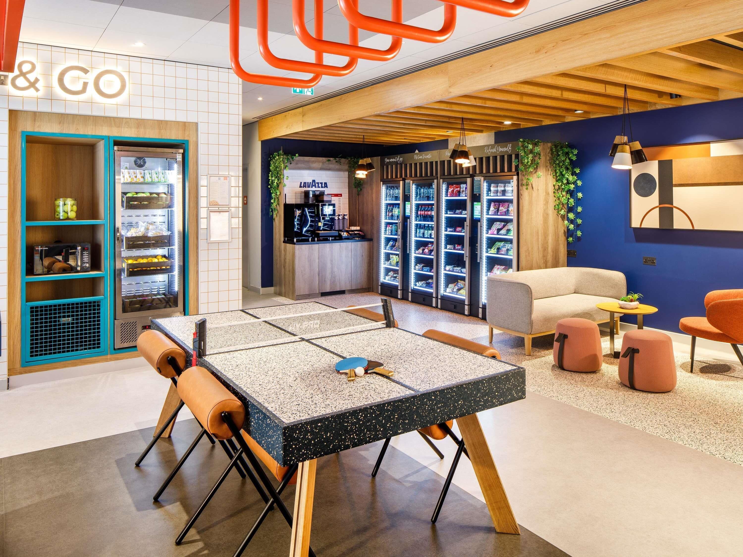 A modern lounge area with a seating arrangement, vending machines, and a counter with a coffee machine.