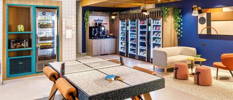 A modern lounge area with a seating arrangement, vending machines, and a counter with a coffee machine.