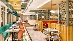 A modern restaurant interior with a long counter, booths, and a mix of seating arrangements. - ibis budget Manchester Airport (Manchester)