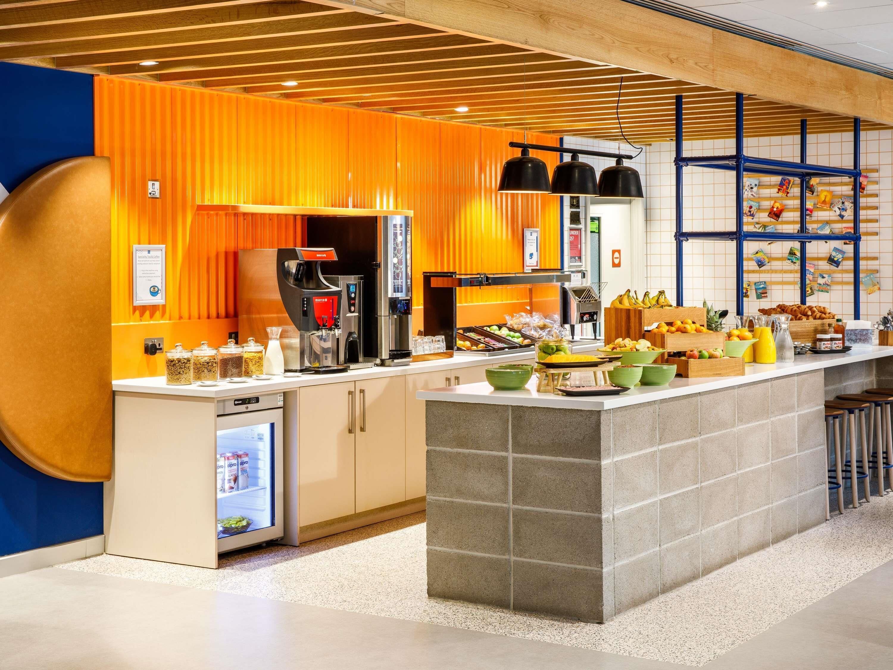 A modern kitchen with a coffee machine, fruit display, and a refrigerator.