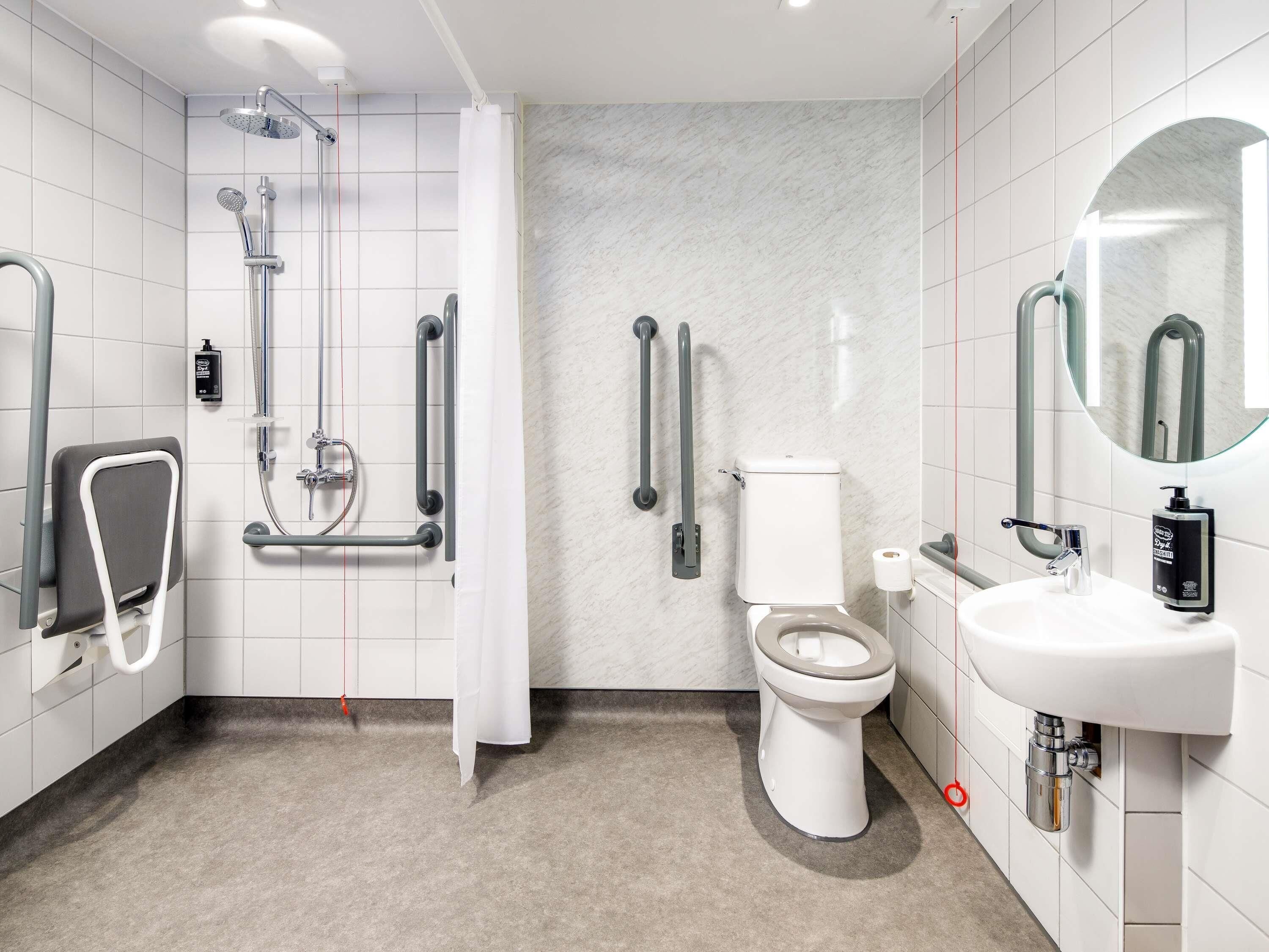 Ein modernes Badezimmer mit Dusche, Toilette und Waschbecken, ausgestattet mit Haltegriffen und einer Handbrause.