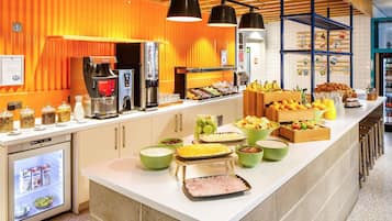 Una barra de desayuno con diferentes alimentos, máquinas de café y un refrigerador.