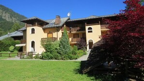A two-story building with a sloped roof, multiple balconies, and a well-maintained garden with various plants and a wooden fence. - 300m from ski lifts, 1st floor, view mountain, balcony, tv, 40m², Les Houches (Les Houches)