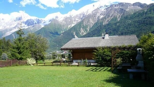 A rustic cabin with a sloped roof, surrounded by a fenced yard and a backdrop of snow-capped mountains. - 300m from ski lifts, 1st floor, view mountain, balcony, tv, 40m², Les Houches (Les Houches)