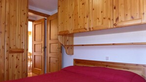 A bedroom with wooden cabinets, a bed with a red blanket, and a wooden headboard. - 300m from ski lifts, 1st floor, view mountain, balcony, tv, 40m², Les Houches (Les Houches)
