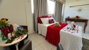 A hotel room with a bed, a small table with flowers, a chair, and a window with curtains. - Pousada Flor De Ponta Negra (Natal)