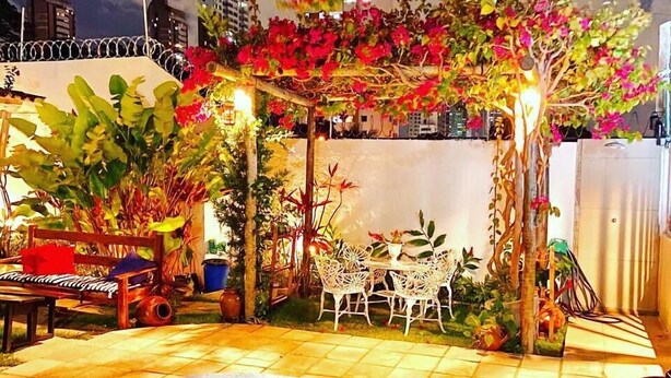 A swimming pool with a tiled deck, surrounded by potted plants and a small table with chairs. - Pousada Flor De Ponta Negra (Natal)