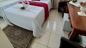 A hotel room with a bed, a desk, and a view of buildings through the window. - Pousada Flor De Ponta Negra (Natal)
