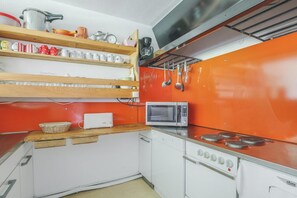 A compact kitchen with a microwave, stove, and shelves with kitchenware.