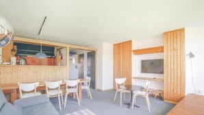 Um espaço compacto com cozinha compacta, área de refeições, sala de estar com sofá e TV fixada na parede.