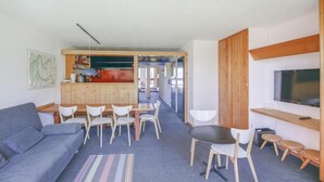 Uma sala de estar moderna com sofá, mesa de jantar, cadeiras, cozinha e televisão.