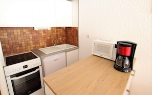 Uma cozinha compacta com micro-ondas, cafeteira, pia e um forno pequeno.