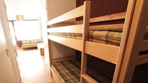 Ein Stockbett mit karierter Matratze in einem Raum mit Holzboden und einer Tür zu einem weiteren Raum.