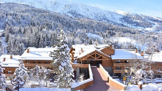 A lodge with a central building, surrounded by snow-covered trees and mountains in the background.
